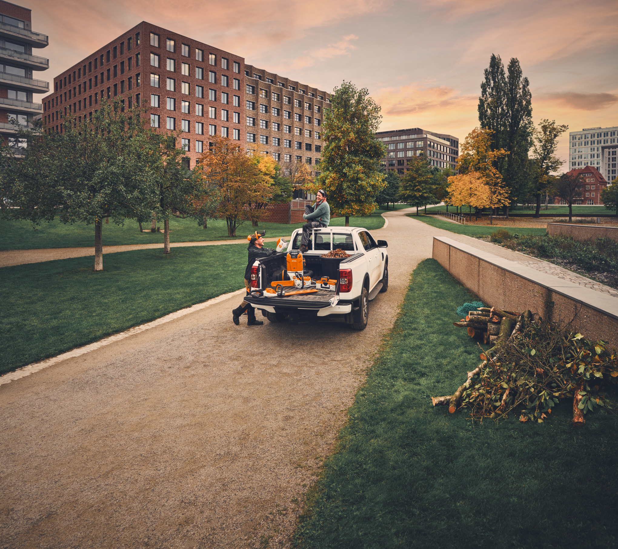 After their work is done, two gardeners and landscapers are on a vehicle with STIHL tools, with cut branches and twigs lying by the side of the path in the foreground