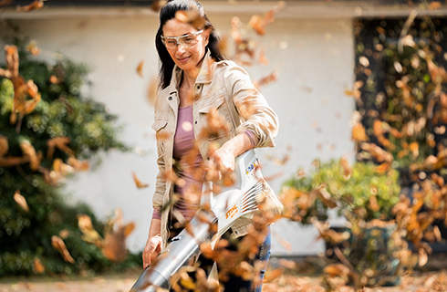 A woman using a STIHL BGA 56 cordless leaf blower to tidy up in spring, with leaves flying up in the foreground