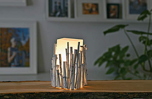 DIY table lamp from twigs: a finished and switched-on lamp on a table, with pictures on a wall in the background