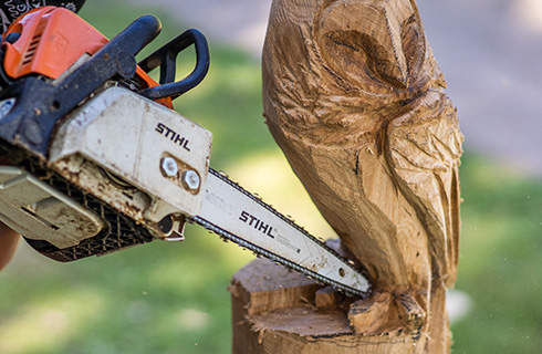 A wooden owl sculpture in progress: a STIHL chainsaw with carving set is used to carve out the wooden owl’s talons.