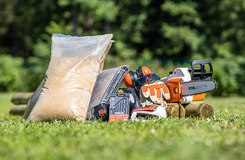 A pile of materials for building a DIY sandpit: STIHL chainsaw, protective equipment, and play sand.