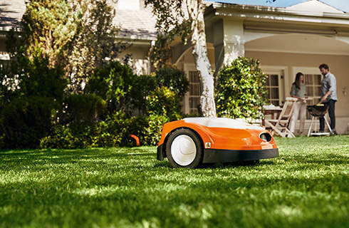STIHL iMOW® RMI 422 robot lawn mower on a green lawn with house and people in the background