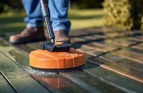 Close-up of the STIHL RA 82 surface cleaner being used to clean wooden decking, with the user’s feet behind it