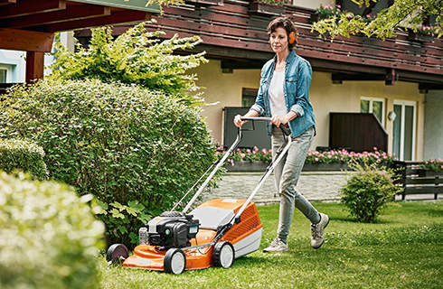 A large, well-tended garden with a bench and swing set in the background, and a man using a STIHL RM 443 petrol-driven lawn mower