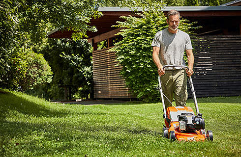 A man mowing a lawn with a STIHL RM 248 petrol lawn mower with a garden shed in the background