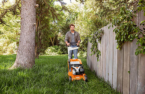A man using a STIHL RM 448 TC petrol lawn mower on grass next to a wooden fence