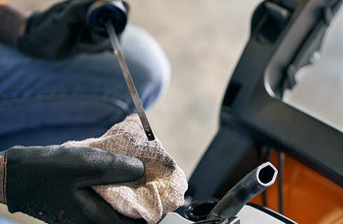 Close-up of a lawn mower dipstick that has been removed from the lawn mower and is being held over a rag to check the oil level