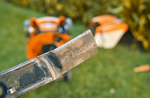 Close-up view of a cutting edge on a lawn mower blade, with an out-of-focus background of a lawn mower on grass