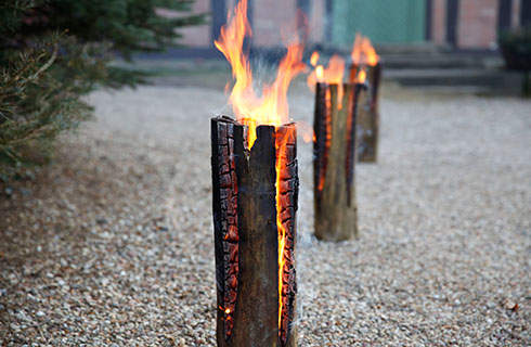 A close-up of the burning top of a Swedish fire log on a gravel path