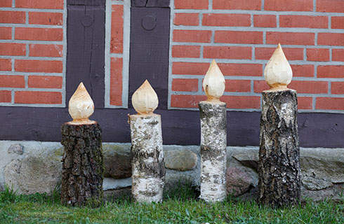 DIY wooden candlesticks: Four candlesticks standing on a lawn in front of a red brick wall