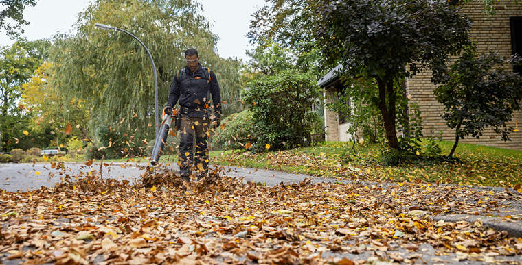 A gardener and landscaper removes leaves from a road using the STIHL BGA 200 cordless leaf blower.