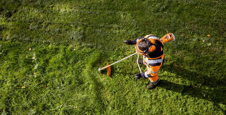 A gardener and landscaper in orange work clothes mows tall grass using the STIHL FSA 135 cordless clearing saw