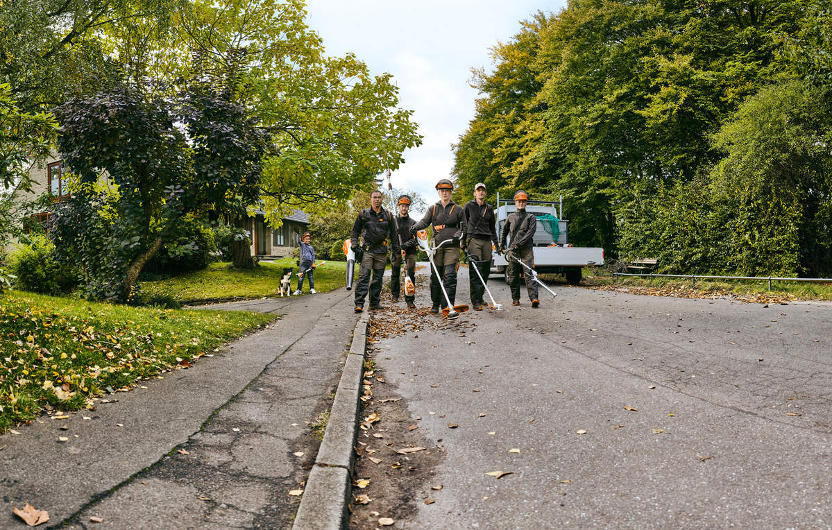 A gardening and landscaping team with STIHL professional cordless power tools walks along a street.