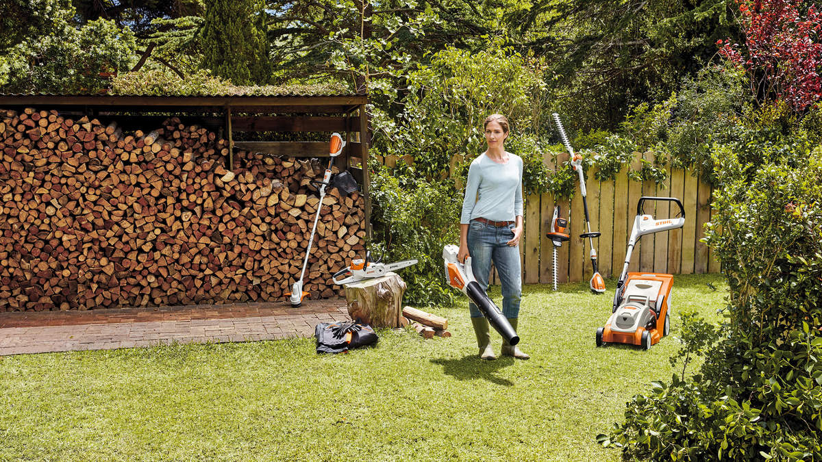 A woman standing in a garden with a selection of STIHL AK System cordless power tools