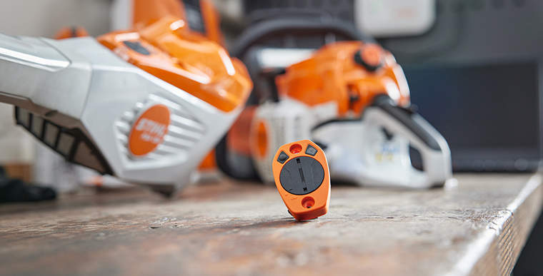 A STIHL Smart Connector and a STIHL Smart Connector 2 A on a workbench. Various STIHL tools can be seen out of focus in the background.