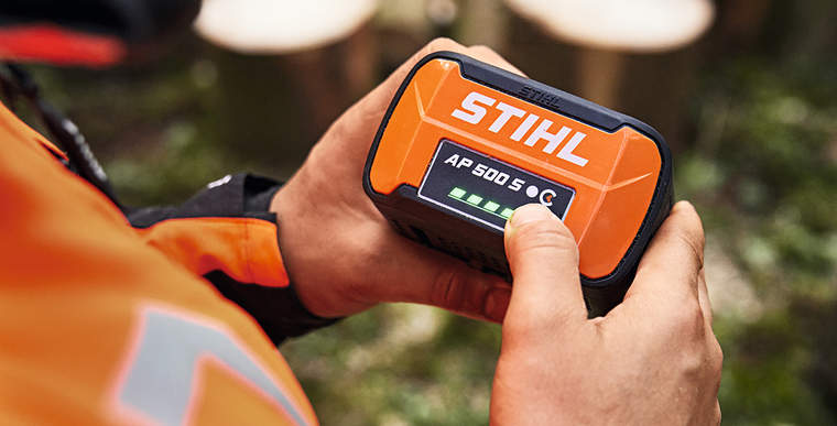 A person holding a STIHL AP 500 S battery in their hands. The LEDs of the charge-level indicator are lit up in green.